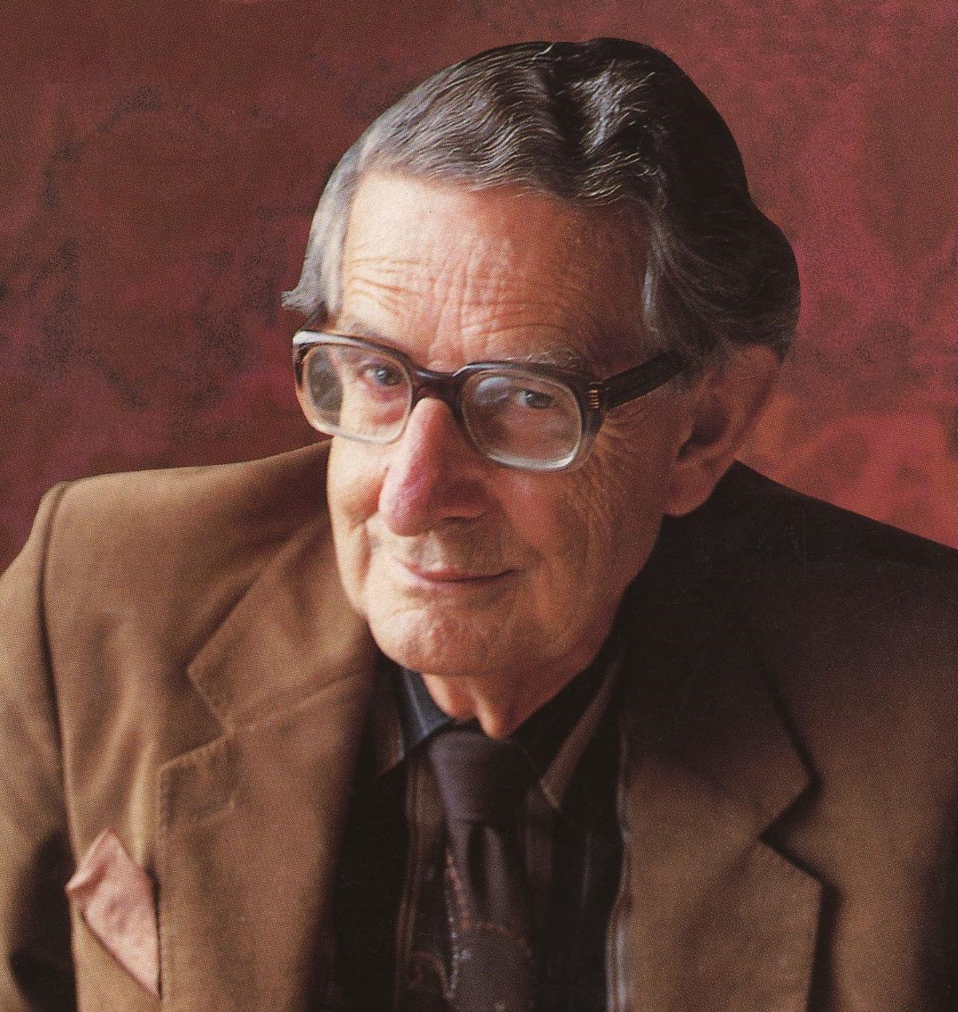 A photograph of Hans Eysenck wearing brown square glasses, a tan blazer, a brown shirt, and a brown tie.