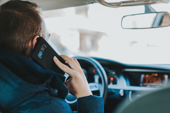 A photograph of a man holding a cell phone to his ear while driving.