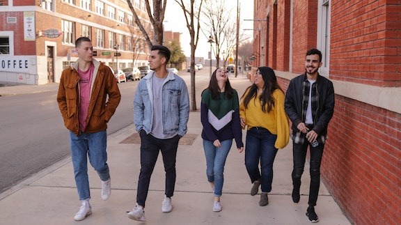 Photo of five young adults walking down a sidewalk, laughing and talking.