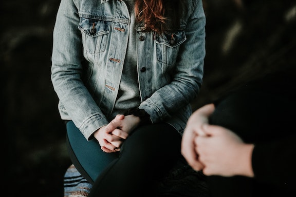 Photo of two people sitting near each other with their hands folded in their laps. Their faces are not visible.